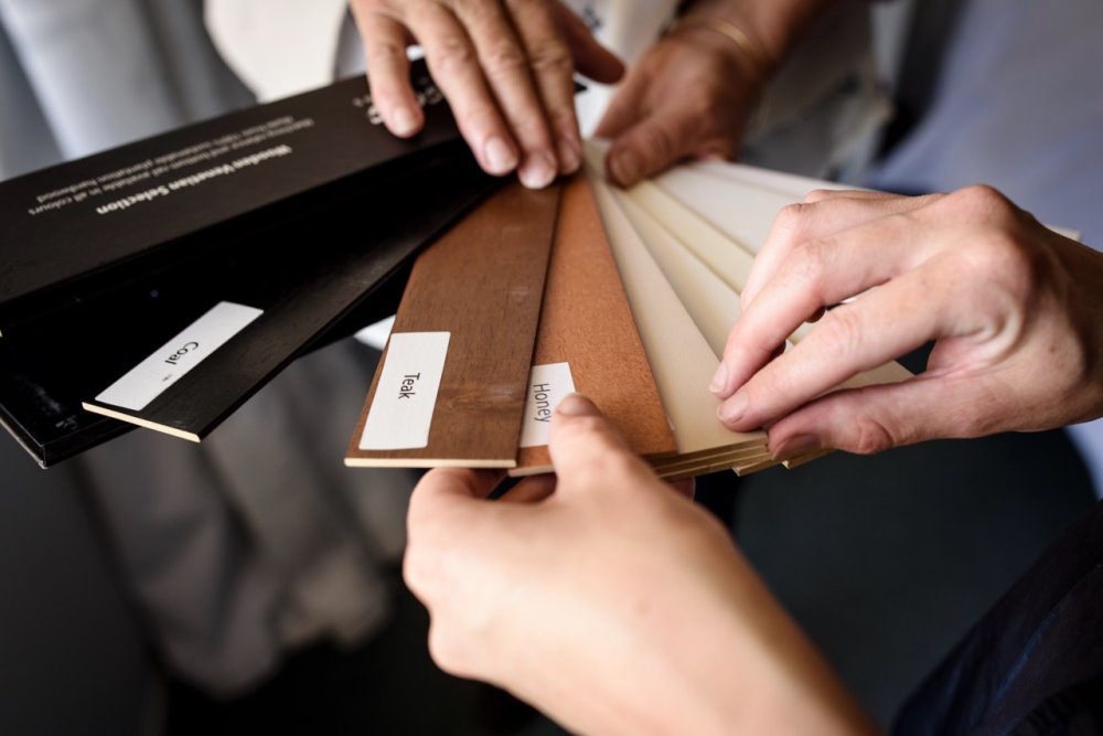 Hands reviewing wood shutter and fabric swatch samples with labels.