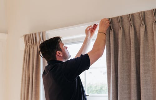 Russells installer installing curtains on curtain rail against window