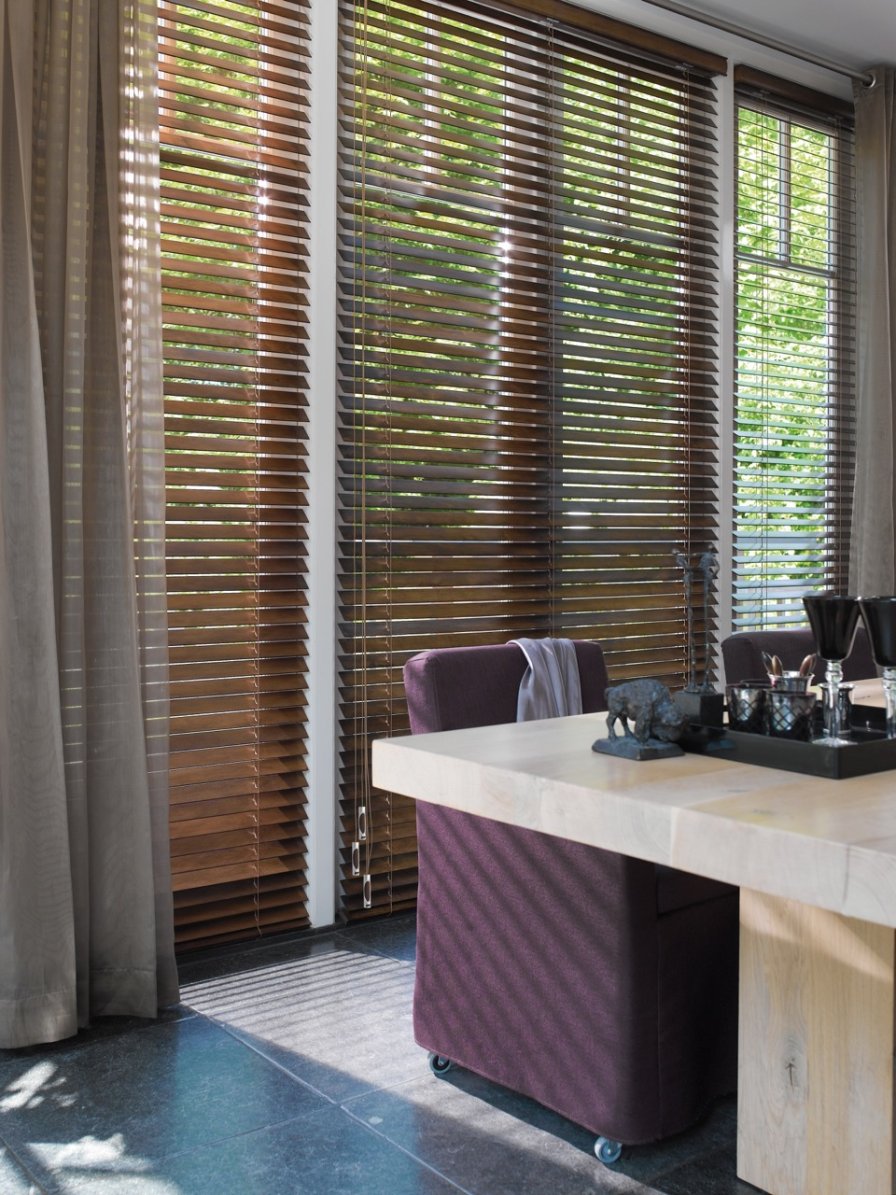 Honey-toned wooden venetian blinds on the windows of a modern bathroom vanity.