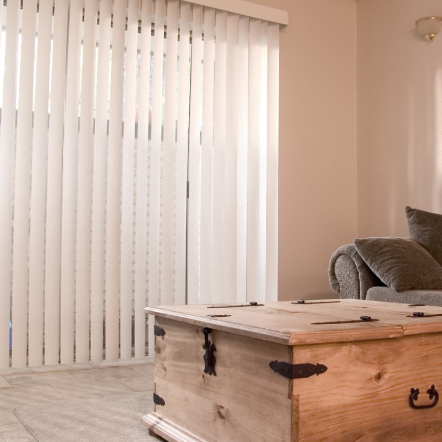 White vertical blinds partly open on a tall window in a neutral room.
