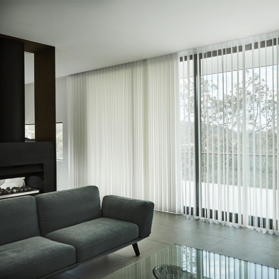 White sheer vertical curtains across floor-to-ceiling sliding doors beside a grey sofa.