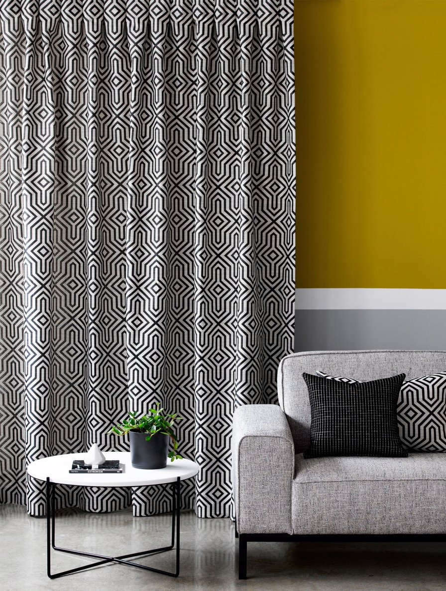 Black and white geometric pencil pleat curtains on a window with a mustard accent wall.