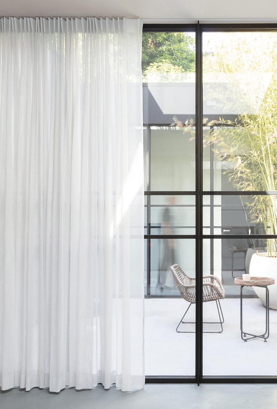 Grey pinch pleat sheer curtains on a ceiling track in a light-filled living space.