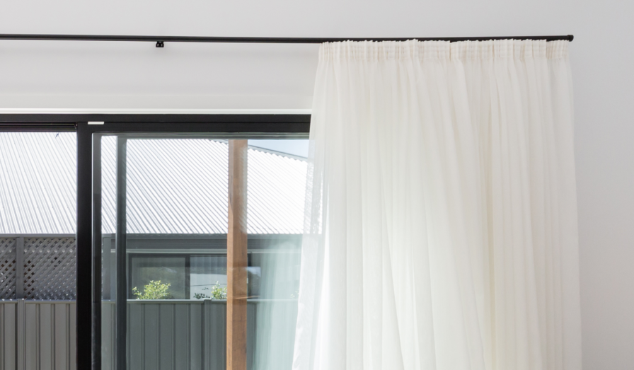 Cream pencil pleat curtains hanging from a black rod.