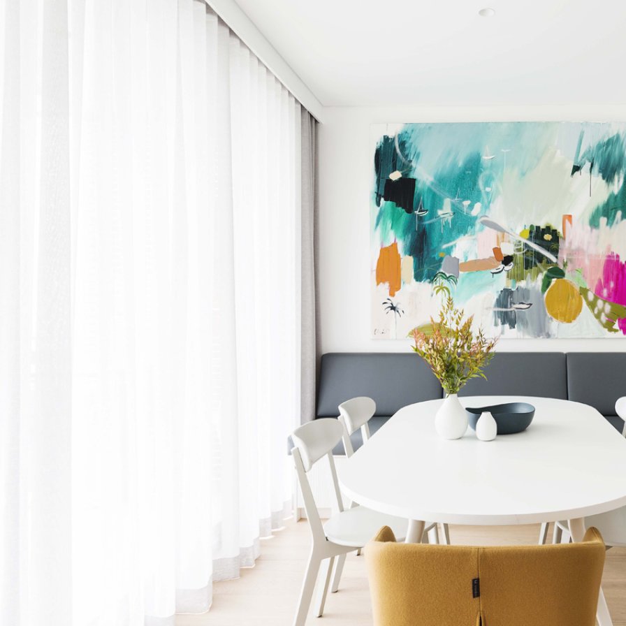 White sheer curtains filtering light in a simple dining nook with a round white table.