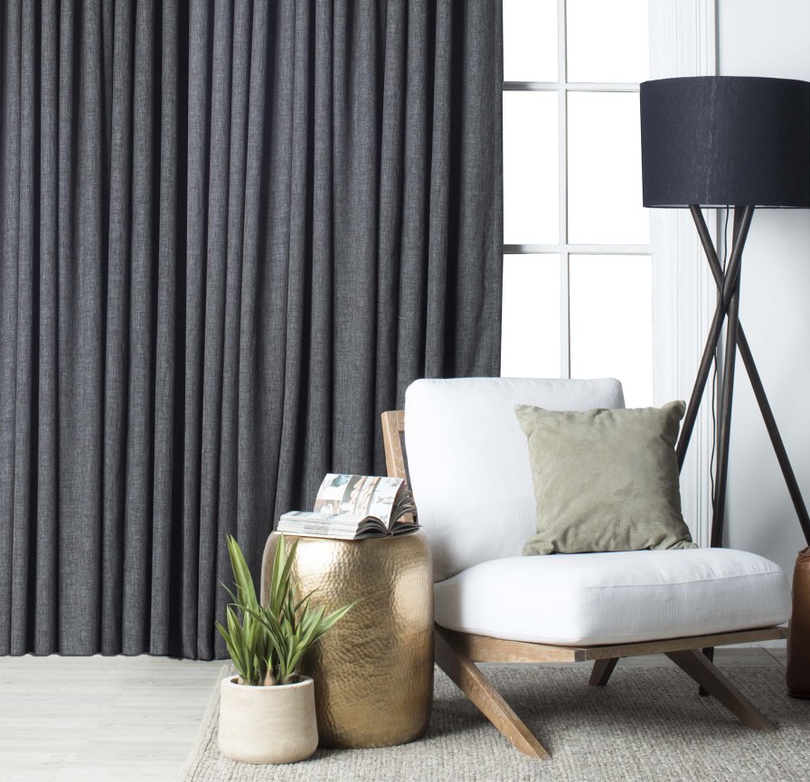 Charcoal pinch pleat curtains on a living-room window with a grey sofa.