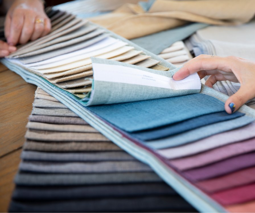 Hands holding stacked curtain fabric swatches in neutral, blue and pink tones.
