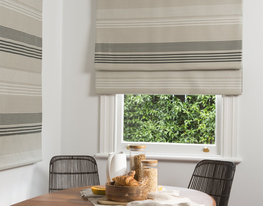Striped roman blind fitted inside a window frame above a dining table with rattan chairs.