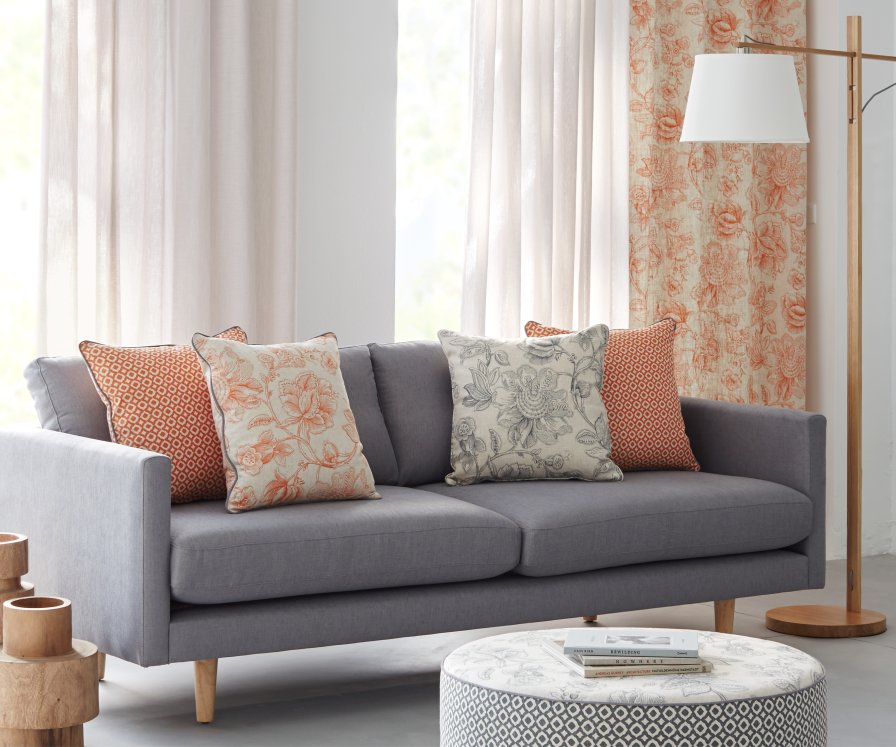 Cream and patterned coral curtains framing a grey sofa with wooden accents.