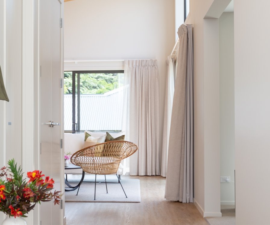 Hallway with pale natural curtains and a roller blind beside a woven basket chair.