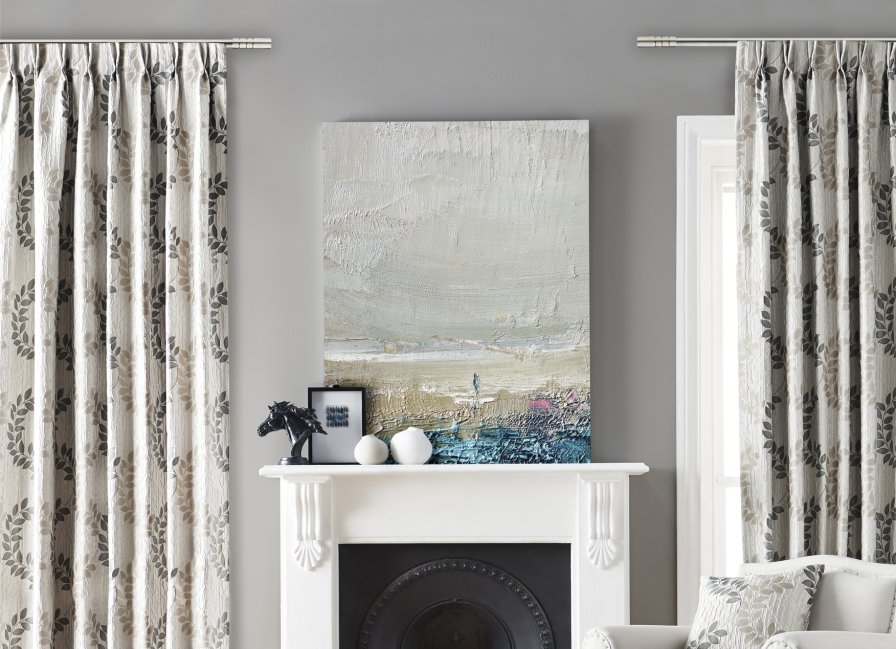 Taupe curtains with a subtle leaf print hanging on either side of a fireplace mantel.