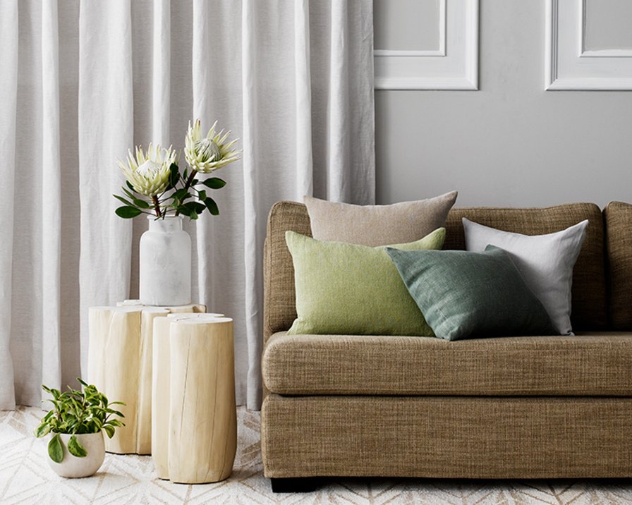 Pale grey linen curtains beside a sofa with pale green and grey cushions.