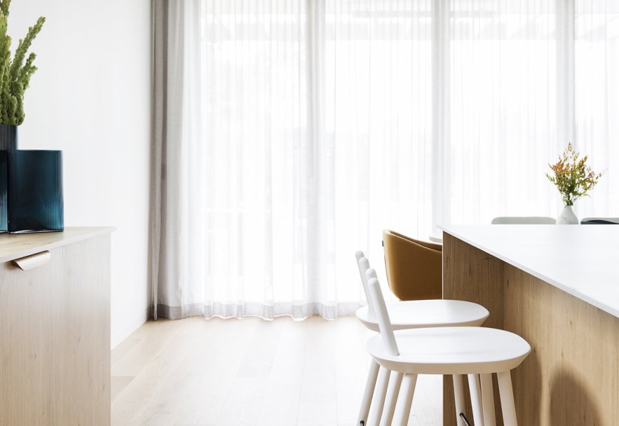 White sheer curtains in a minimalist dining area with wooden furniture and plants.