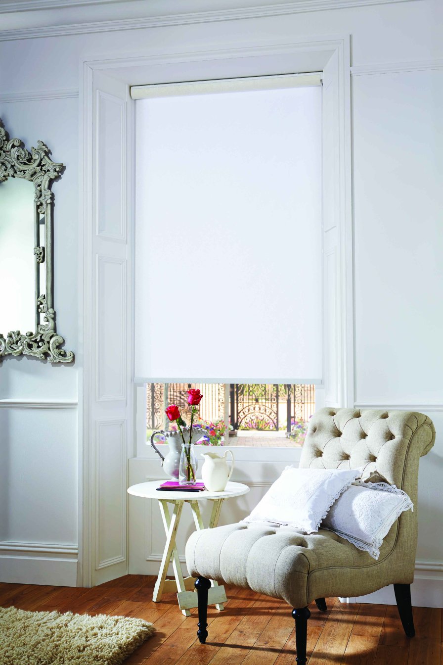 White blockout roller blind fully closed over a window beside a floral vase.