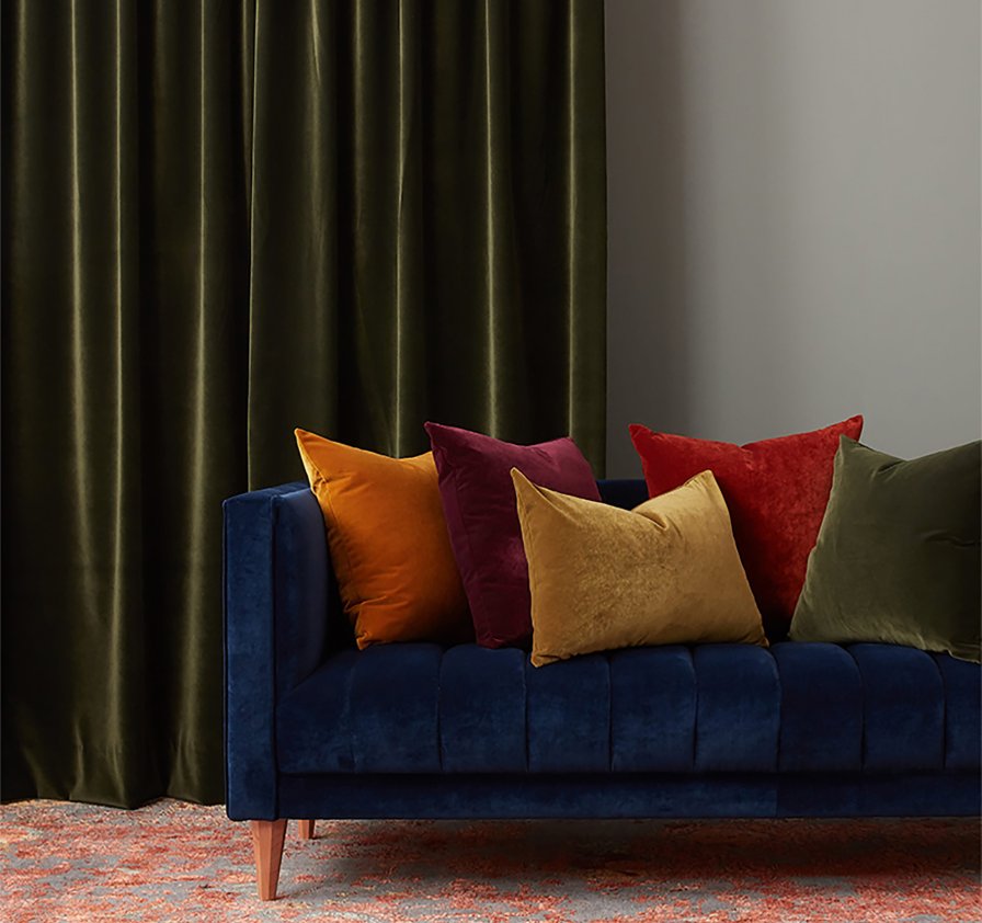 Dark olive-green velvet curtains with jewel-toned cushions on a navy sofa.