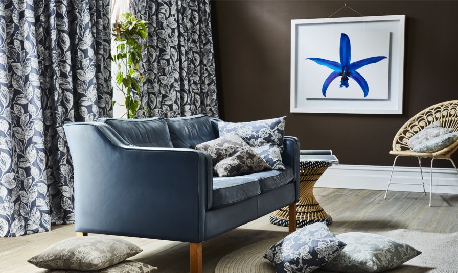 Modern living room with black and white botanical curtains, a navy sofa and rattan pieces.