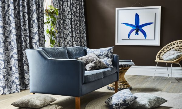 Modern living room with black and white botanical curtains, a navy sofa and rattan pieces.