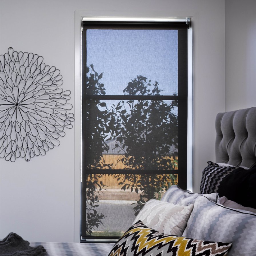 Black sunscreen roller blind on a corner window with garden foliage visible through it.