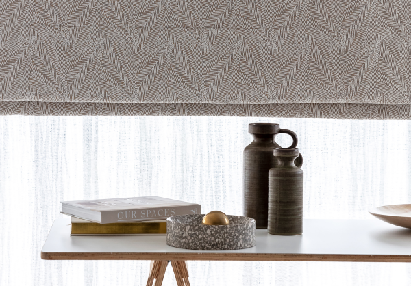 Close-up of a grey geometric-pattern roman blind layered above a white linen shade.