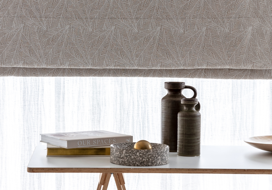 Close-up of a grey geometric-pattern roman blind layered above a white linen shade.