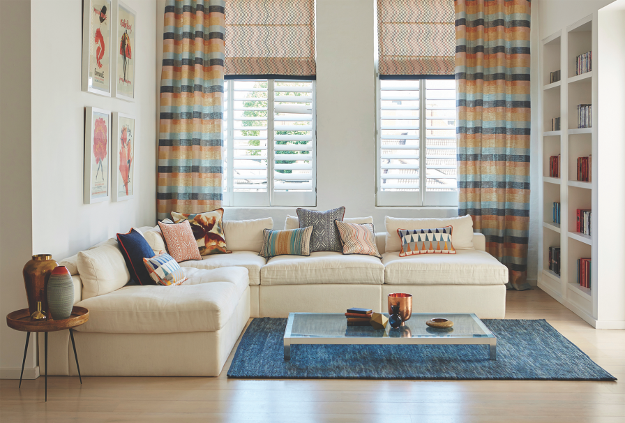 Living room layering coral, blush and denim striped curtains with white plantation shutters.