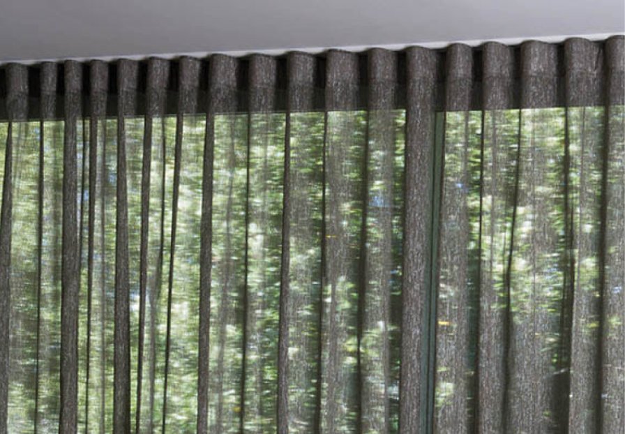 Dark grey textured eyelet curtains on a pole, showing the vertical pleats and rings.