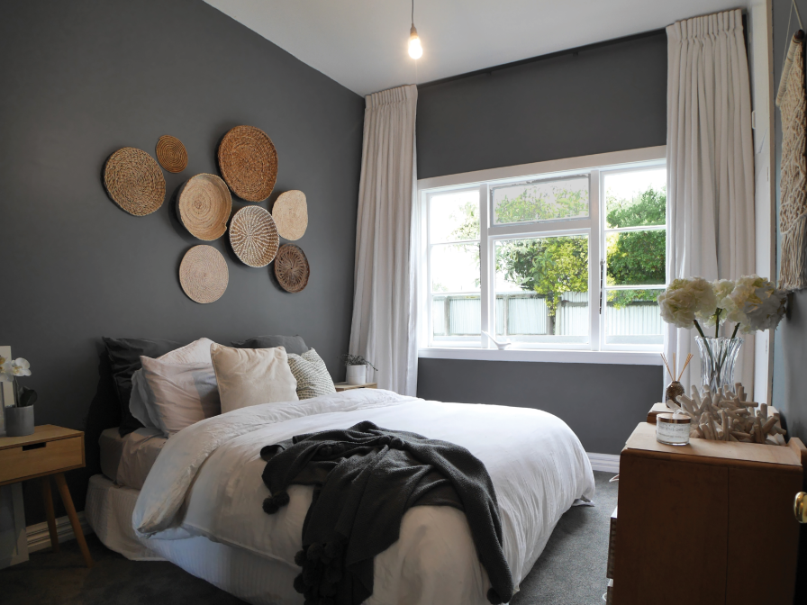 Bedroom with pale grey ceiling-mounted curtains beside an arched window above wall art.