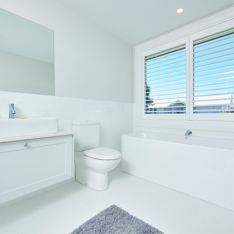 White plantation shutters on a bathroom window above a white tub and vanity.