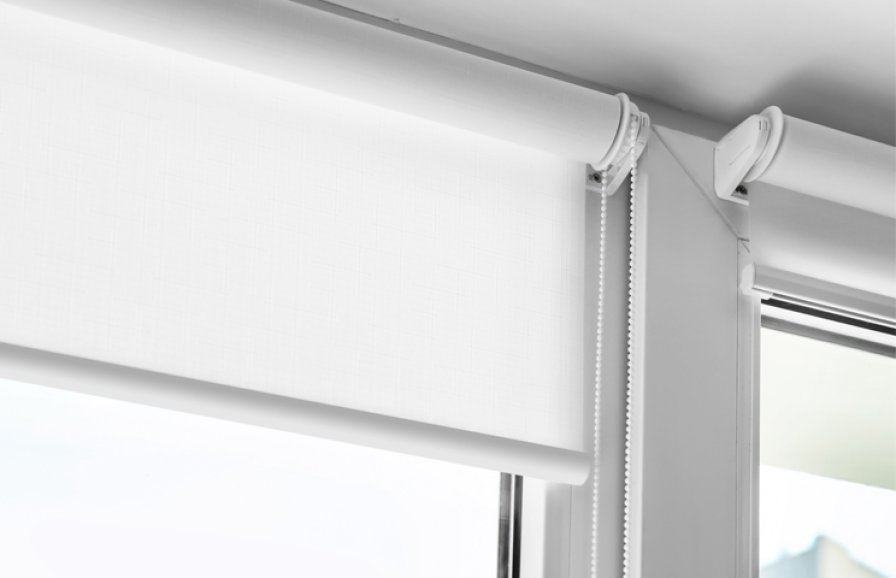 Close-up of a white roller blind's control chain against a bright bathroom window.