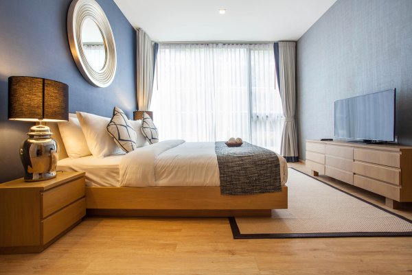Bright bedroom with pale wood furniture and layered grey and white sheer curtains.