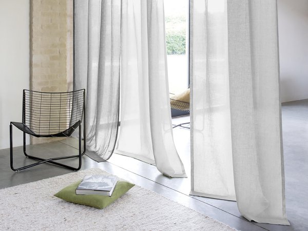 Living room with floor-to-ceiling white sheer curtains and greenery visible outside.