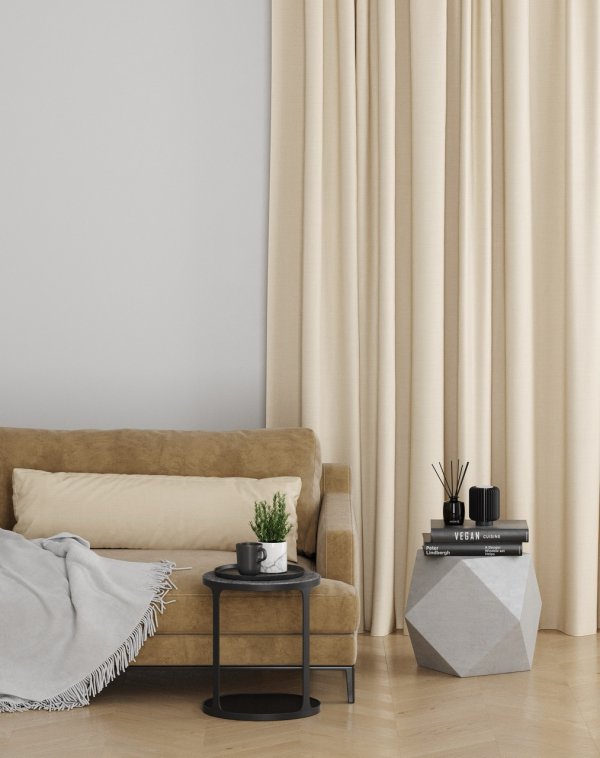 Cream s-fold curtains beside a bed with mustard and cream cushions and wood furniture.