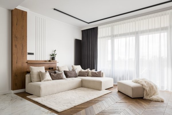 Modern living room with a cream sofa and charcoal and white sheer curtains by a wood accent wall.