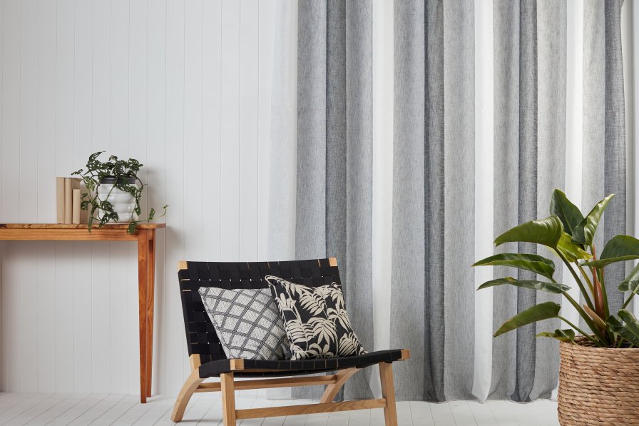 Grey and white vertical-stripe curtains by a wooden accent wall with a black lounge chair.