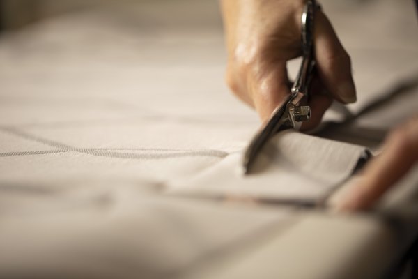A hand cutting cream curtain fabric with large tailor's shears.