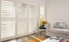 White timber shutters on living-room windows beside a cream sofa and wooden coffee table.
