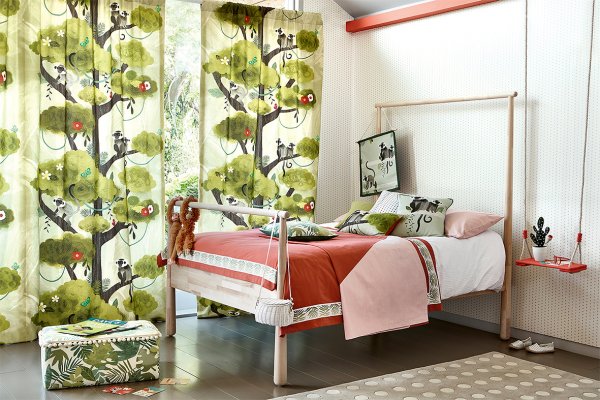 Curtains with a playful monkey and botanical print in a child's bedroom with a white metal bed.