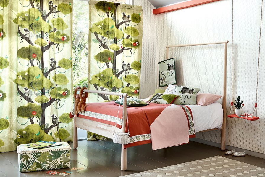 Curtains with a playful monkey and botanical print in a child's bedroom with a white metal bed.