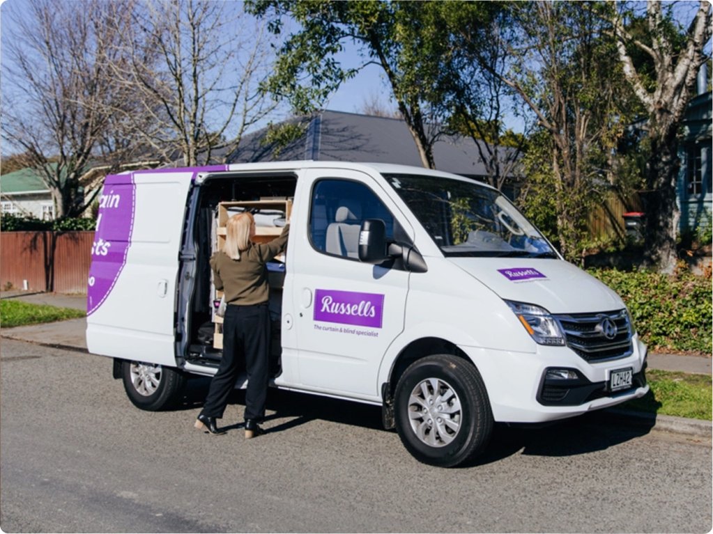A Russells consultant loading curtain and blind samples into a branded van on a suburban street.