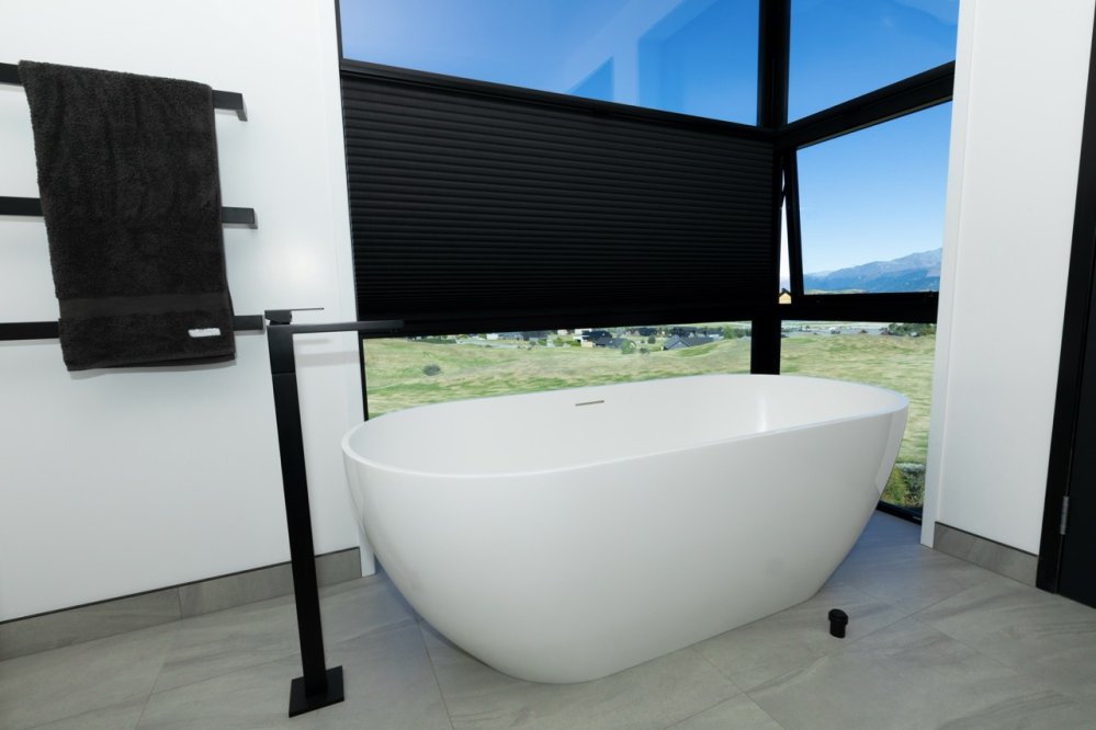Black roller blinds with a mountain view in a contemporary bathroom with a white freestanding tub.