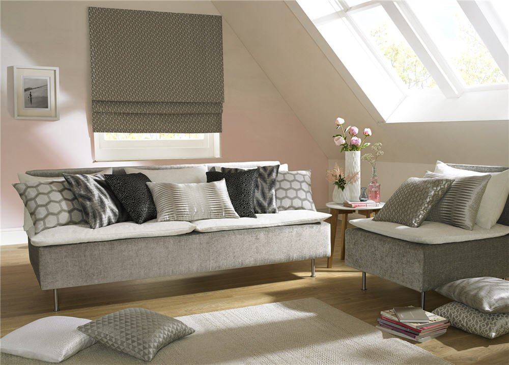 Taupe patterned roman blind above a window in an attic living room with grey sofas and cushions.