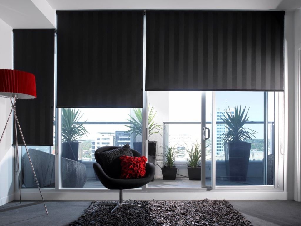 Black blockout roller blind in a modern living room overlooking timber decking and garden.