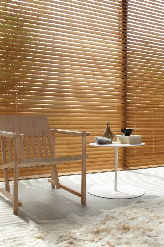 Light honey wooden venetian blinds by a sunny outdoor patio with seating.