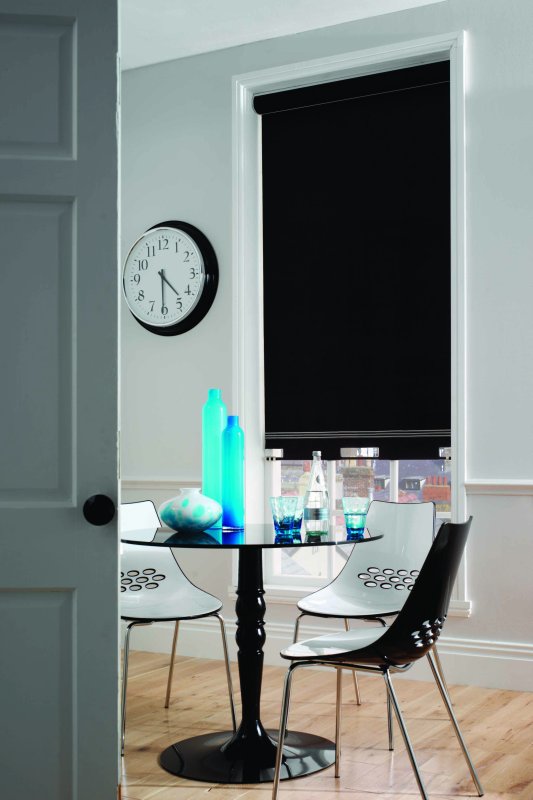 Black blockout roller blind fully lowered on a window in a light bedroom.