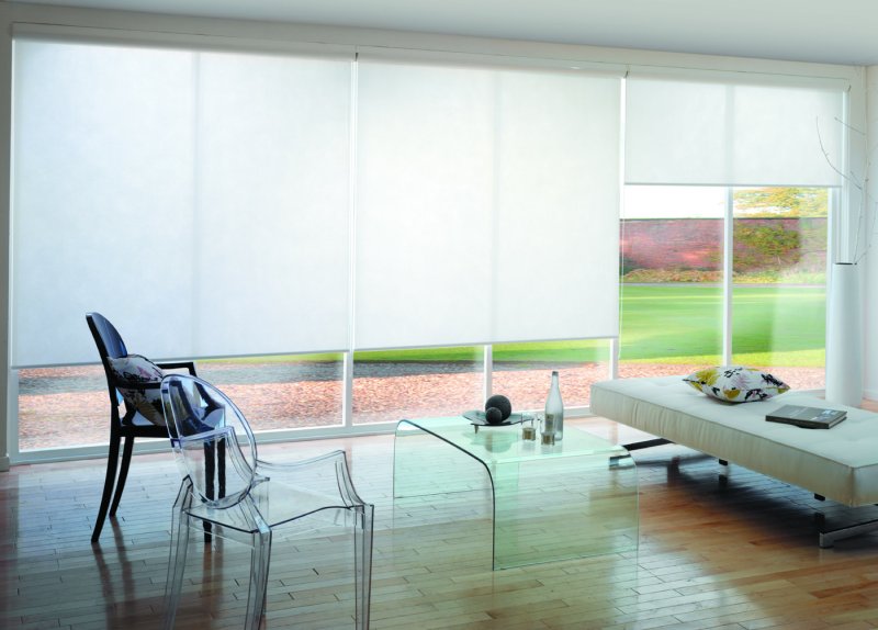 White sunscreen roller blinds on large windows in an open-plan room overlooking the landscape.