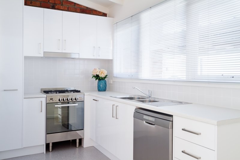 White roller blinds on a kitchen window with white metro tiles and stainless appliances.