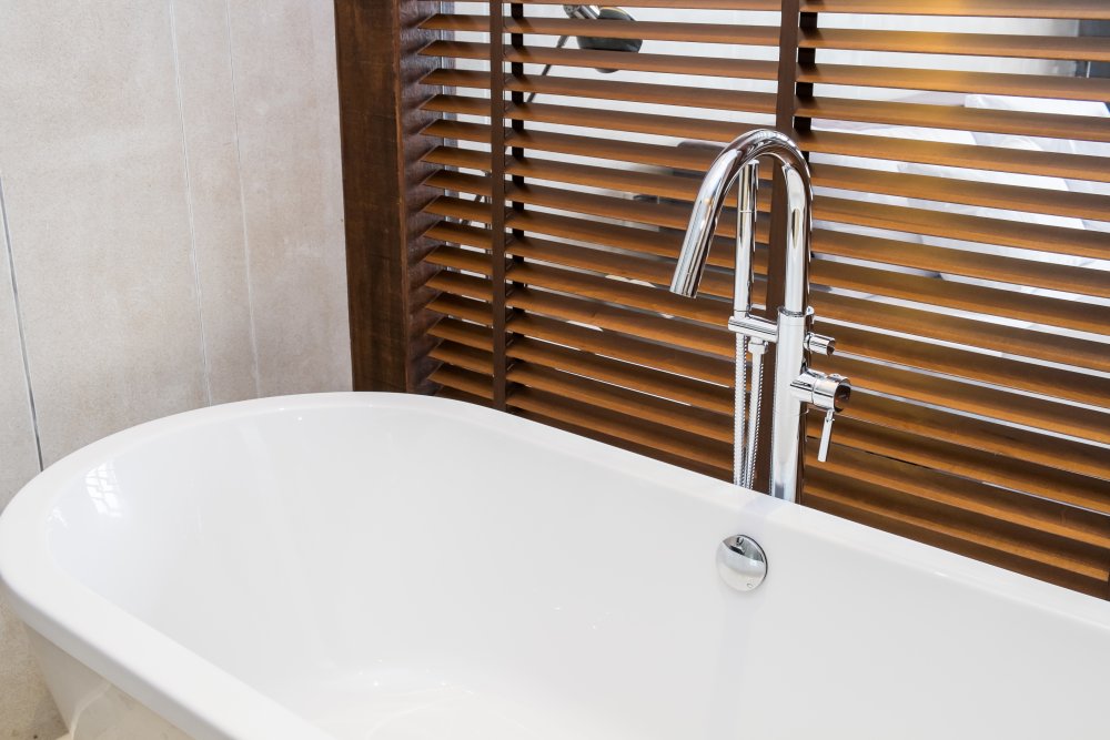 Mid-brown wooden venetian blinds in a modern bathroom overlooking a white tub.