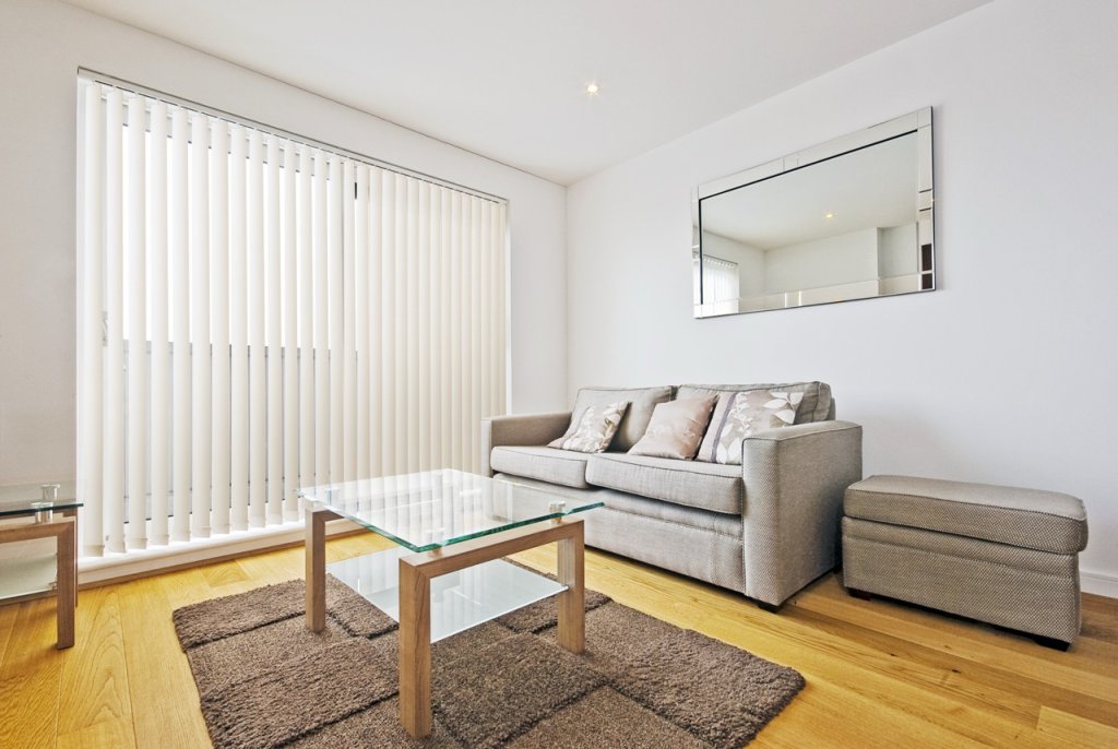 White vertical blinds on a large living-room window with a modern sofa.