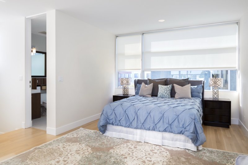 White roller blinds on bedroom windows behind a bed with blue bedding.