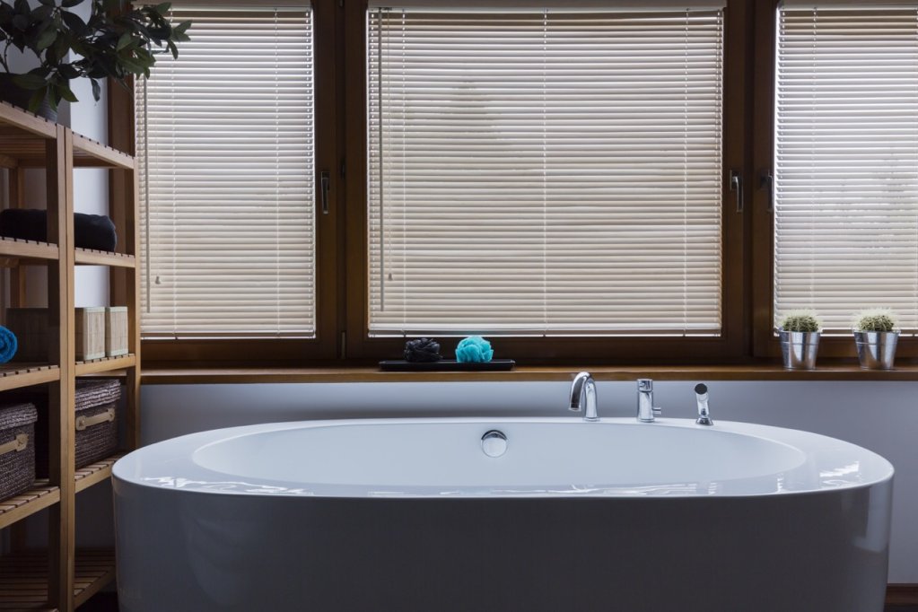 White horizontal slat blinds on bathroom windows above a soaking tub.